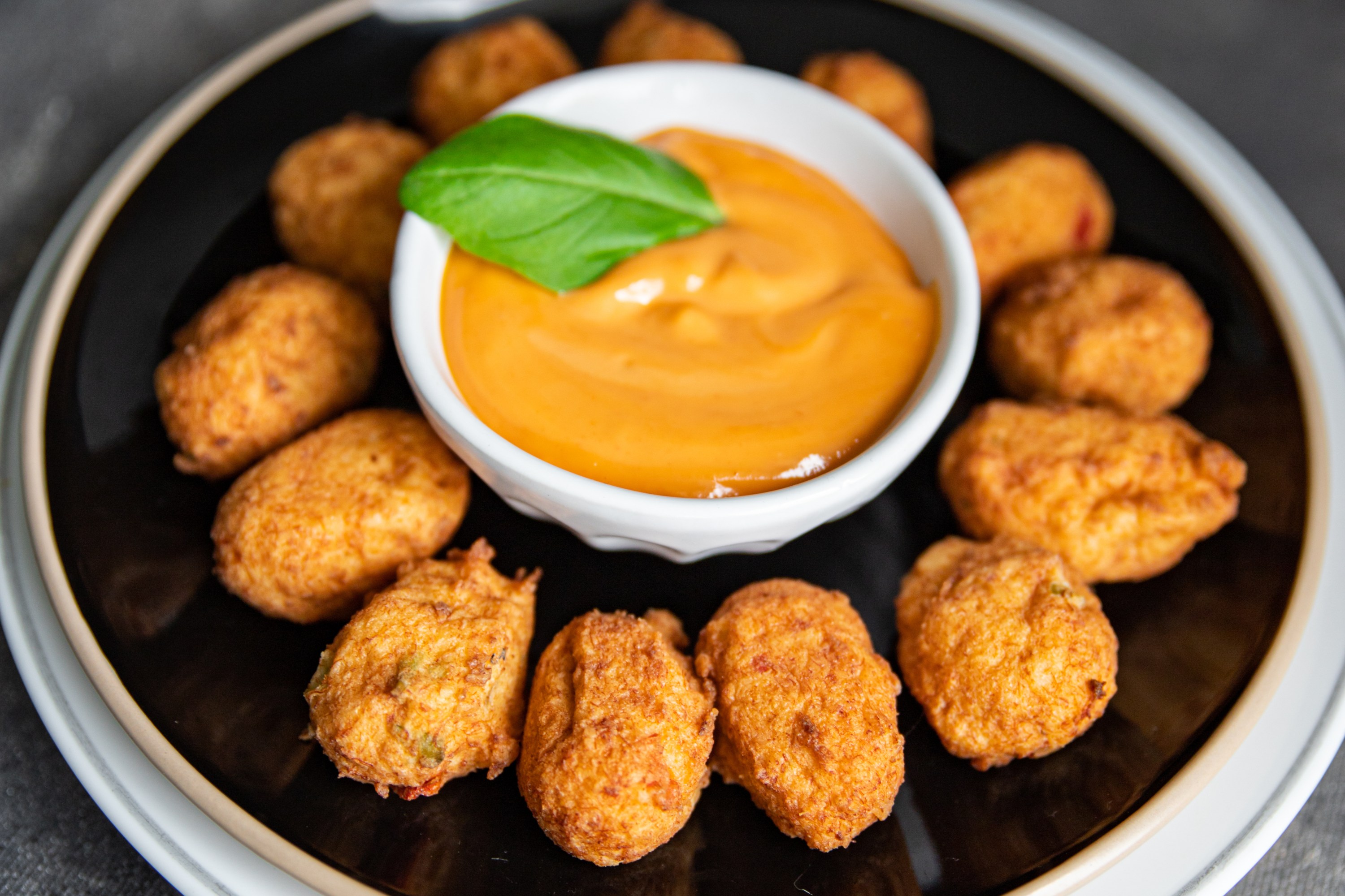 Plate of fried snacks with dip in the center, garnished with a basil leaf.