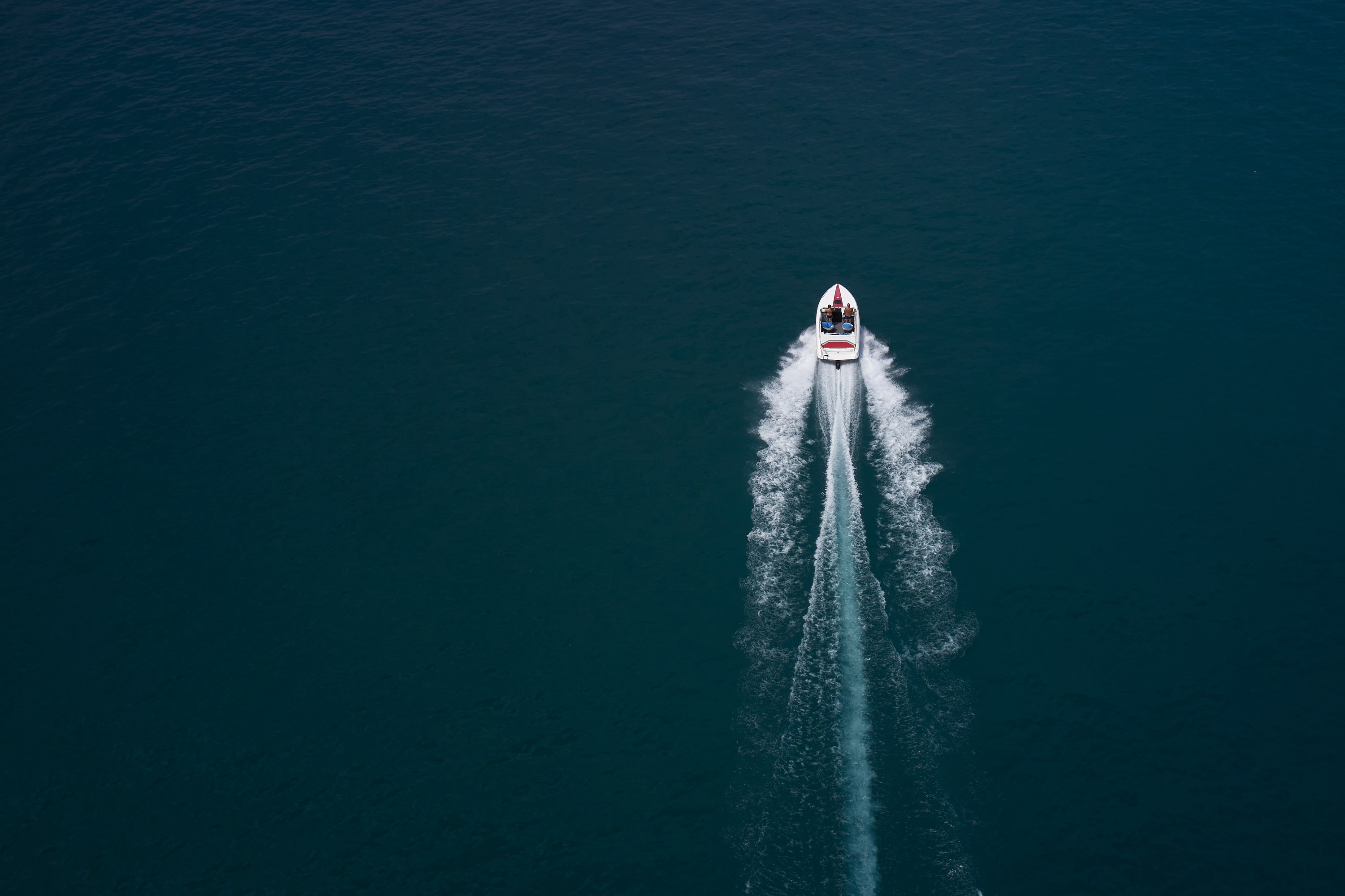 Aerial view of a speedboat creating a wake on dark blue water.