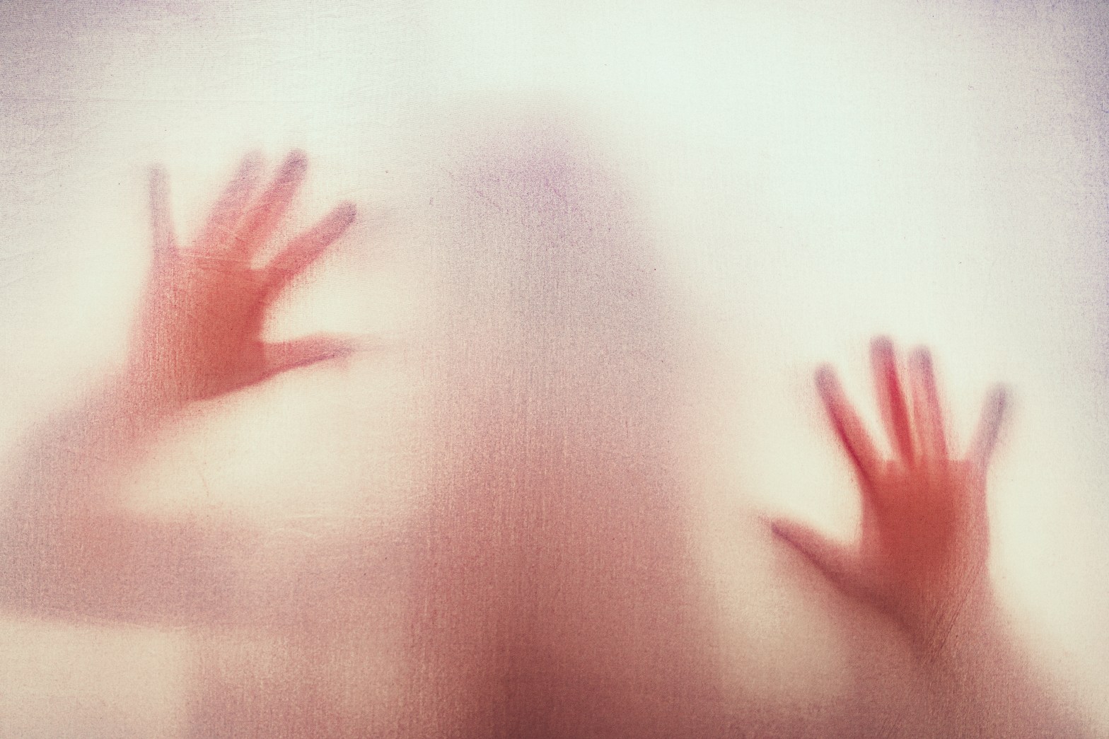 Blurred silhouette of hands and a person behind frosted glass.