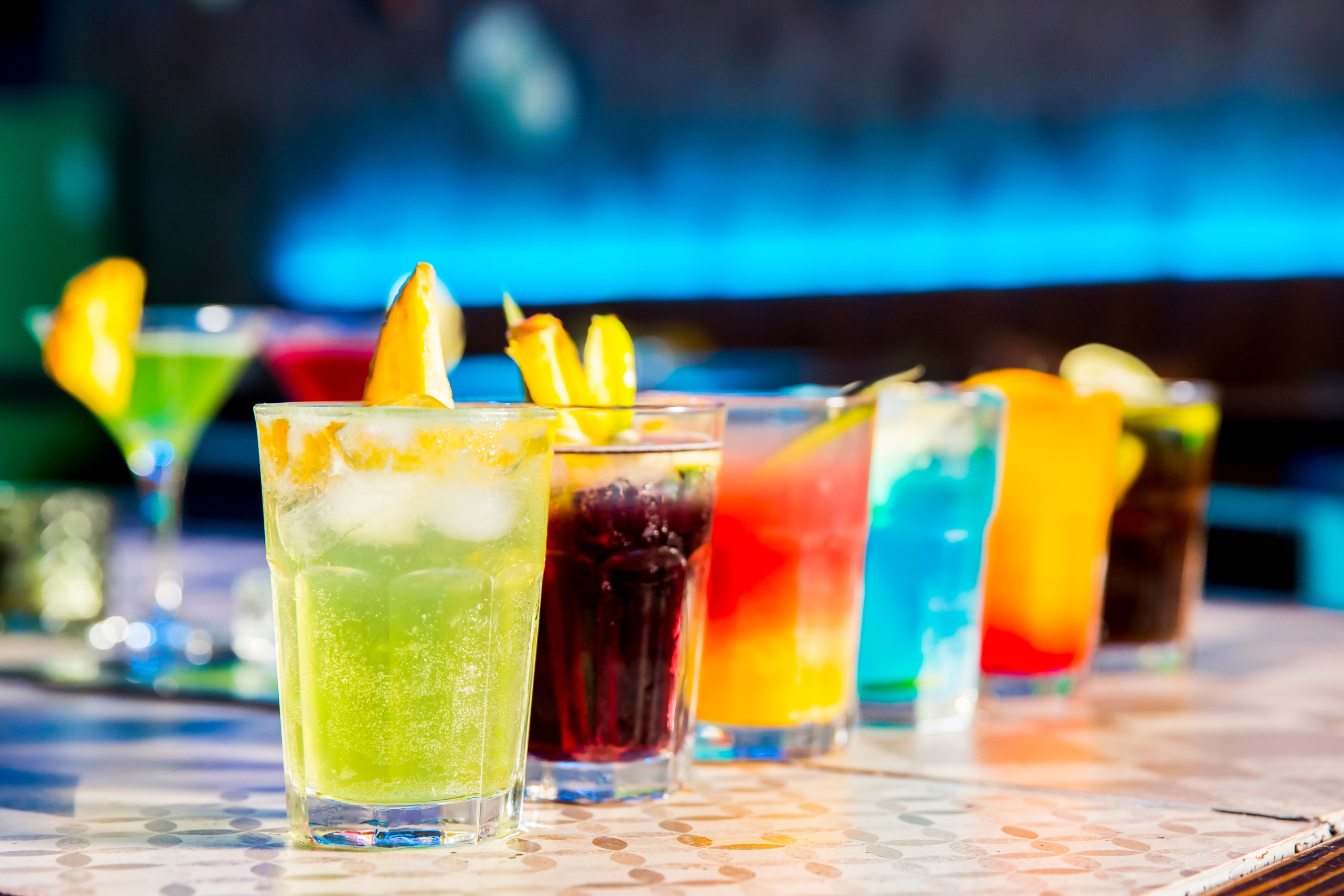 A row of colorful cocktails on a bar counter with bright lighting.