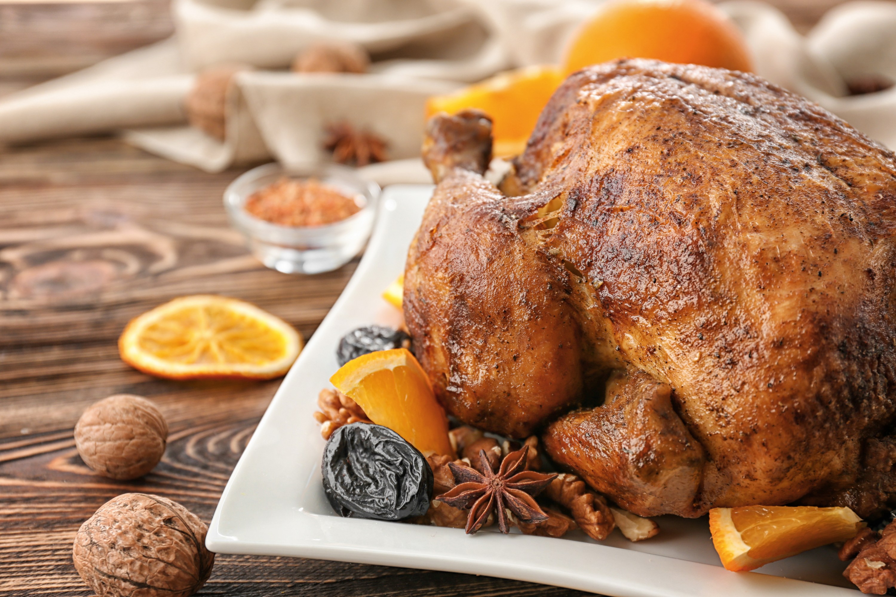 Roasted chicken on a plate with oranges, prunes, walnuts, and star anise.