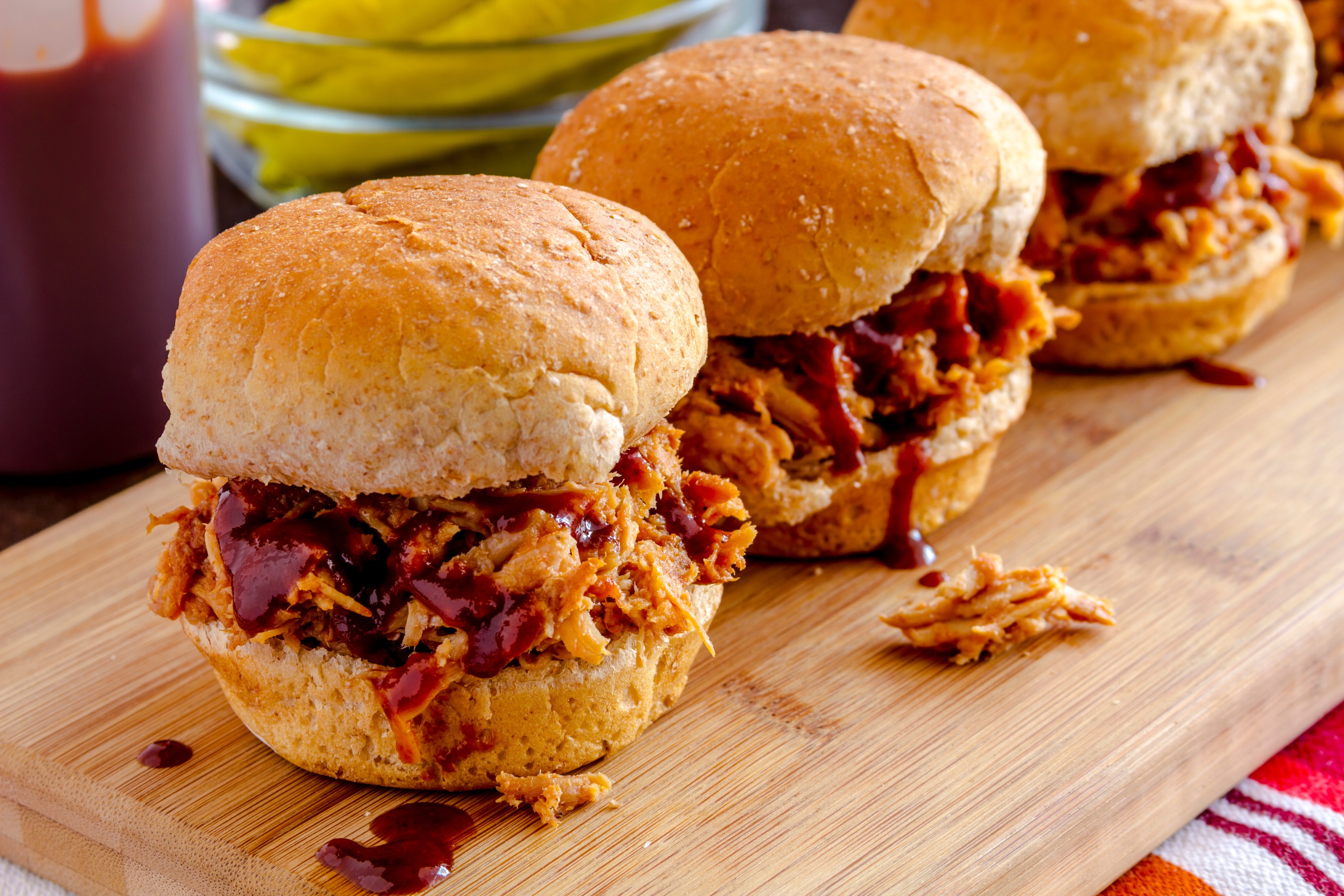 Three pulled pork sliders with BBQ sauce on a wooden board.