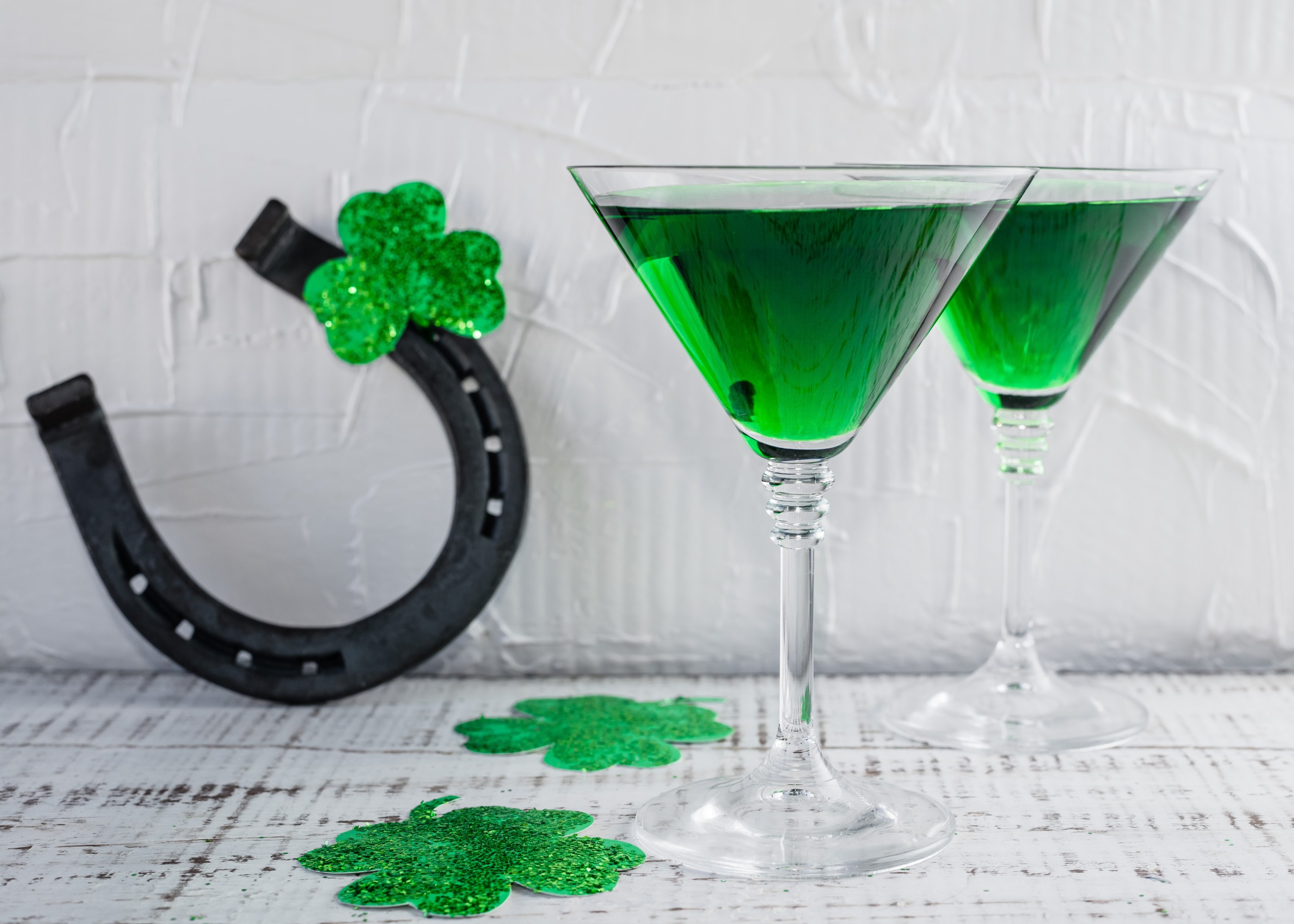 Two green cocktails in martini glasses with clover and horseshoe decor on a textured surface.