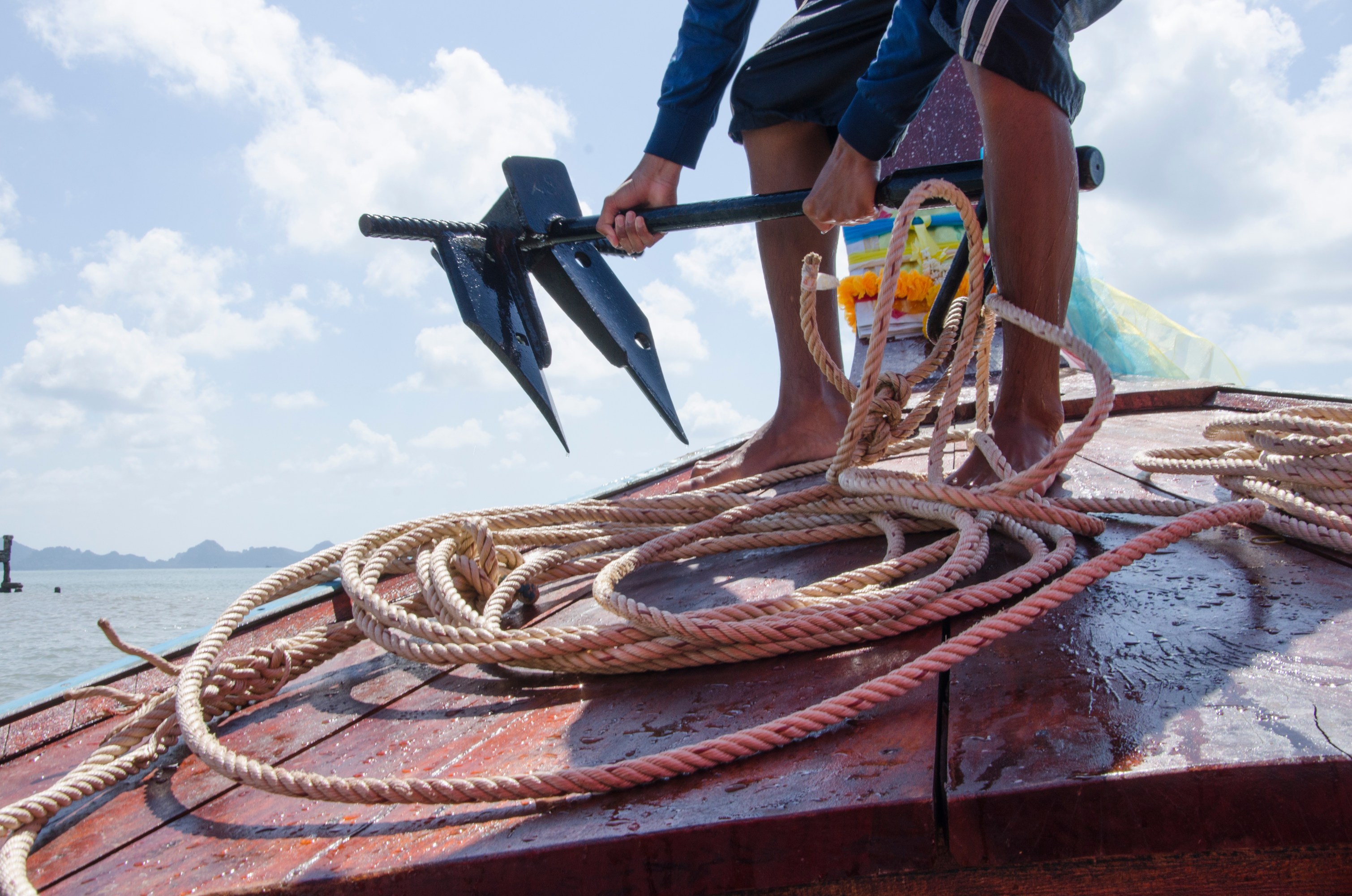 Person holding an anchor with ropes on a boat under a cloudy sky.