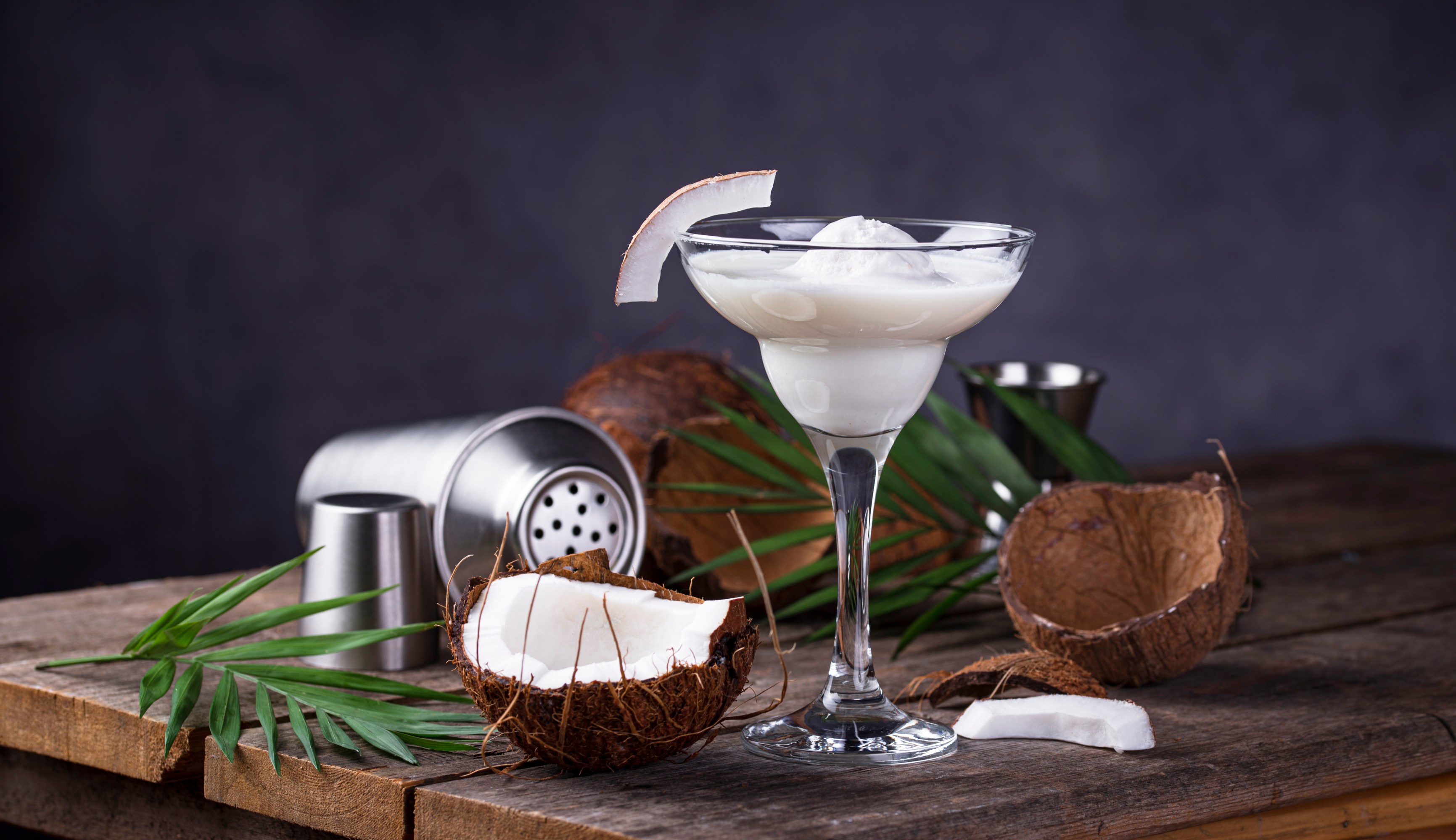 Coconut cocktail in a glass with coconut halves and shaker on a rustic table.