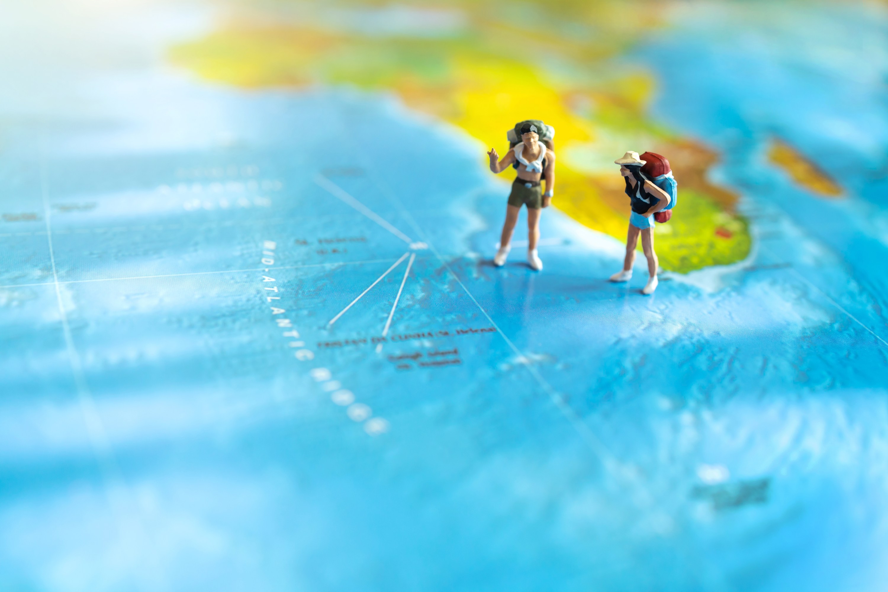 Two miniature figures with backpacks on a world map, suggesting travel.