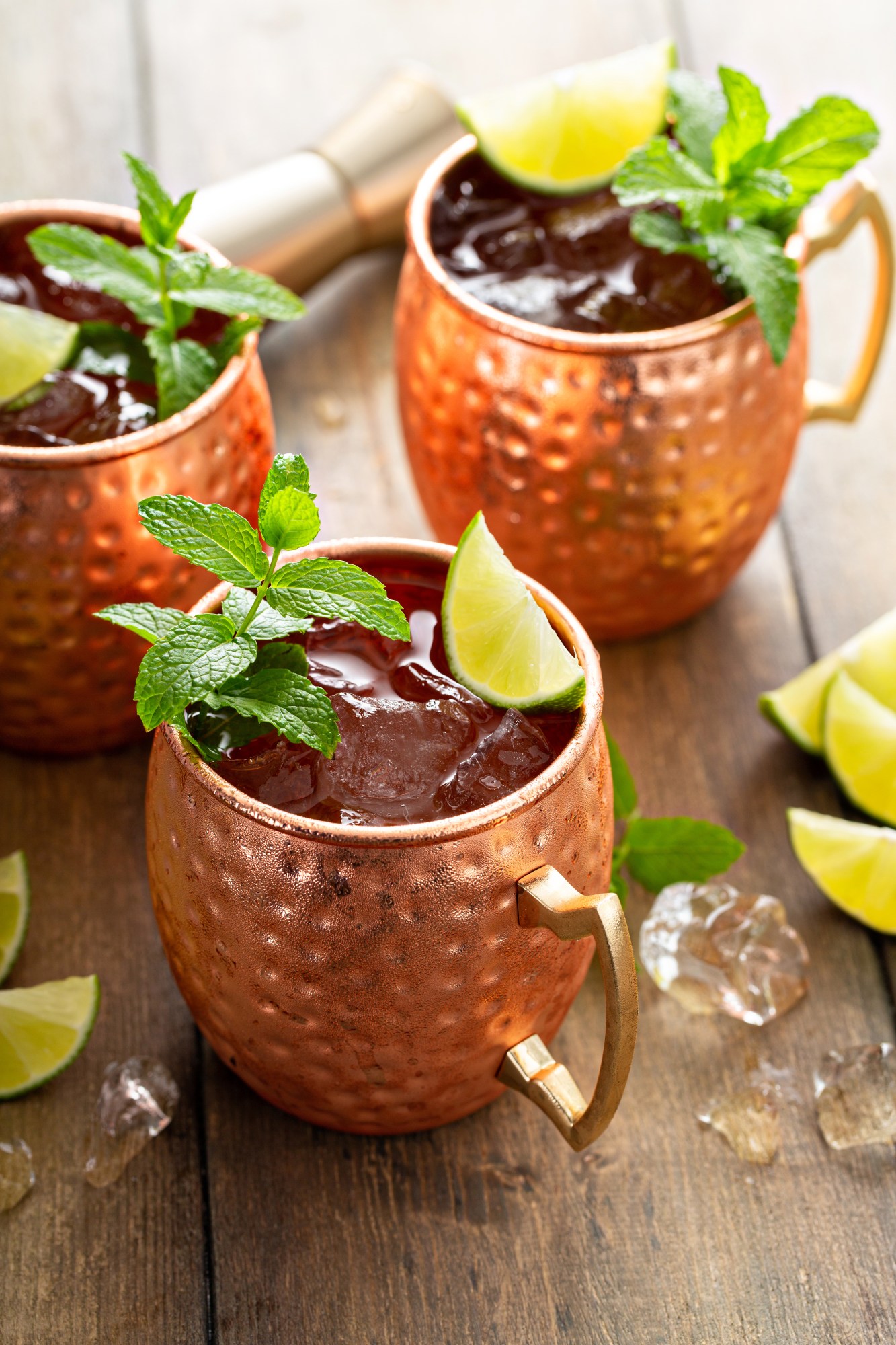 Three copper mugs with drinks, lime wedges, and mint sprigs on a wooden table.