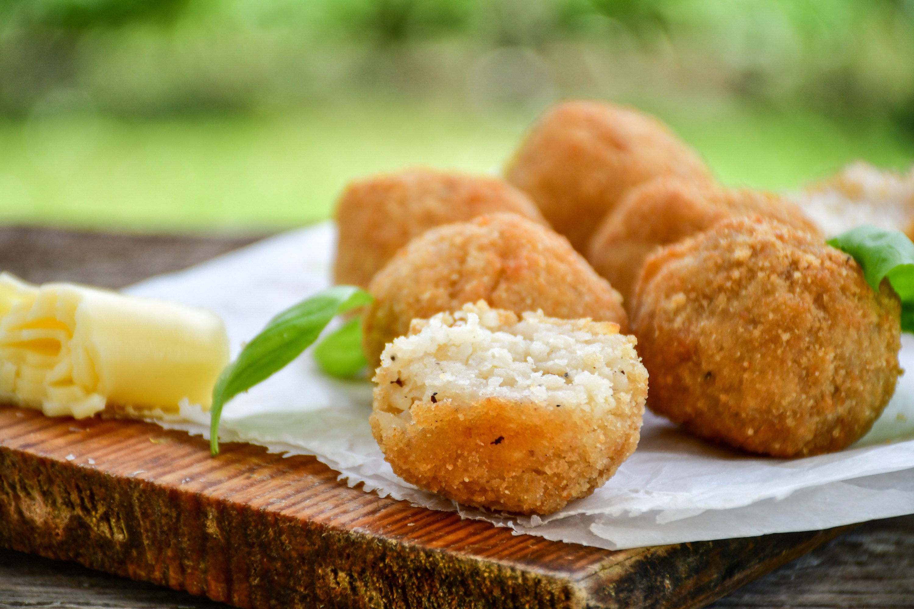 Close-up of fried arancini balls and grated cheese on a wooden board.