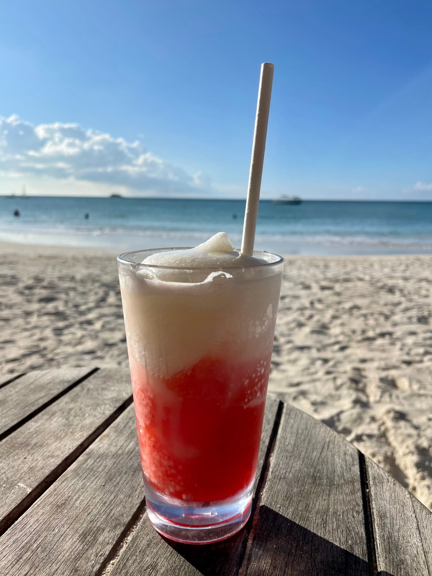 A layered red and white frosty drink on a table by the beach.