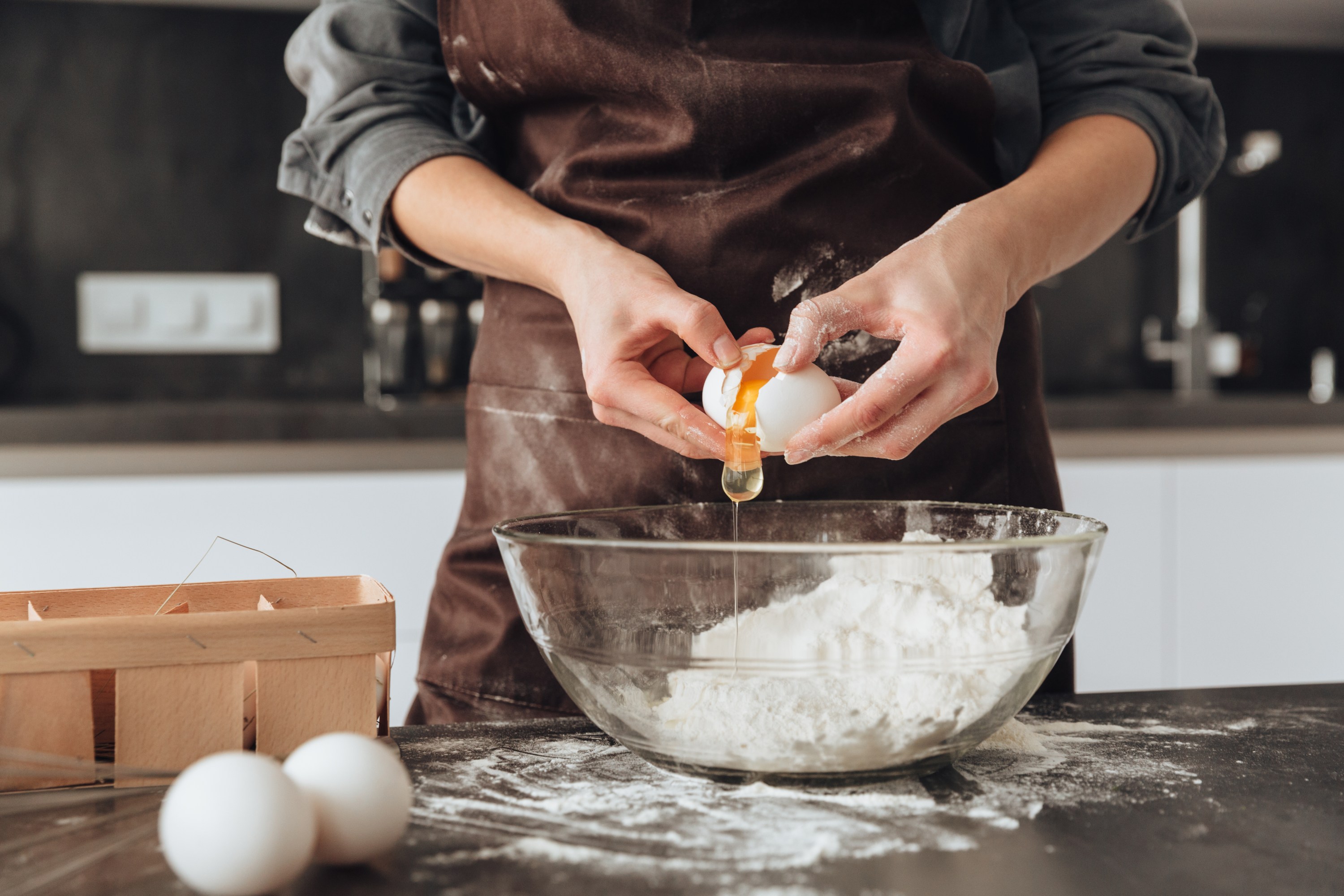 Person cracking an egg into a bowl of flour in a kitchen setting.
