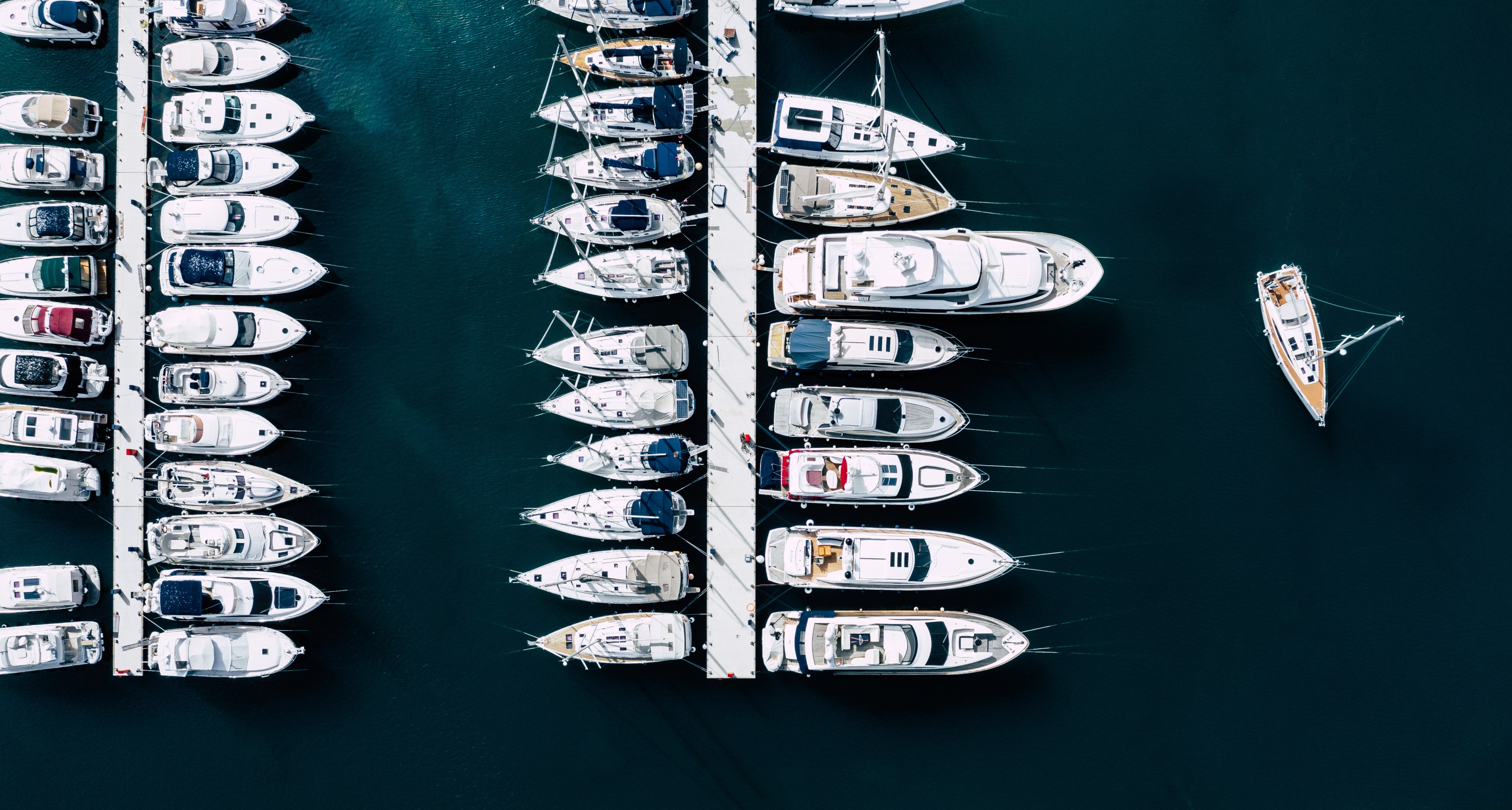 Aerial view of boats docked at a marina with one boat sailing nearby.