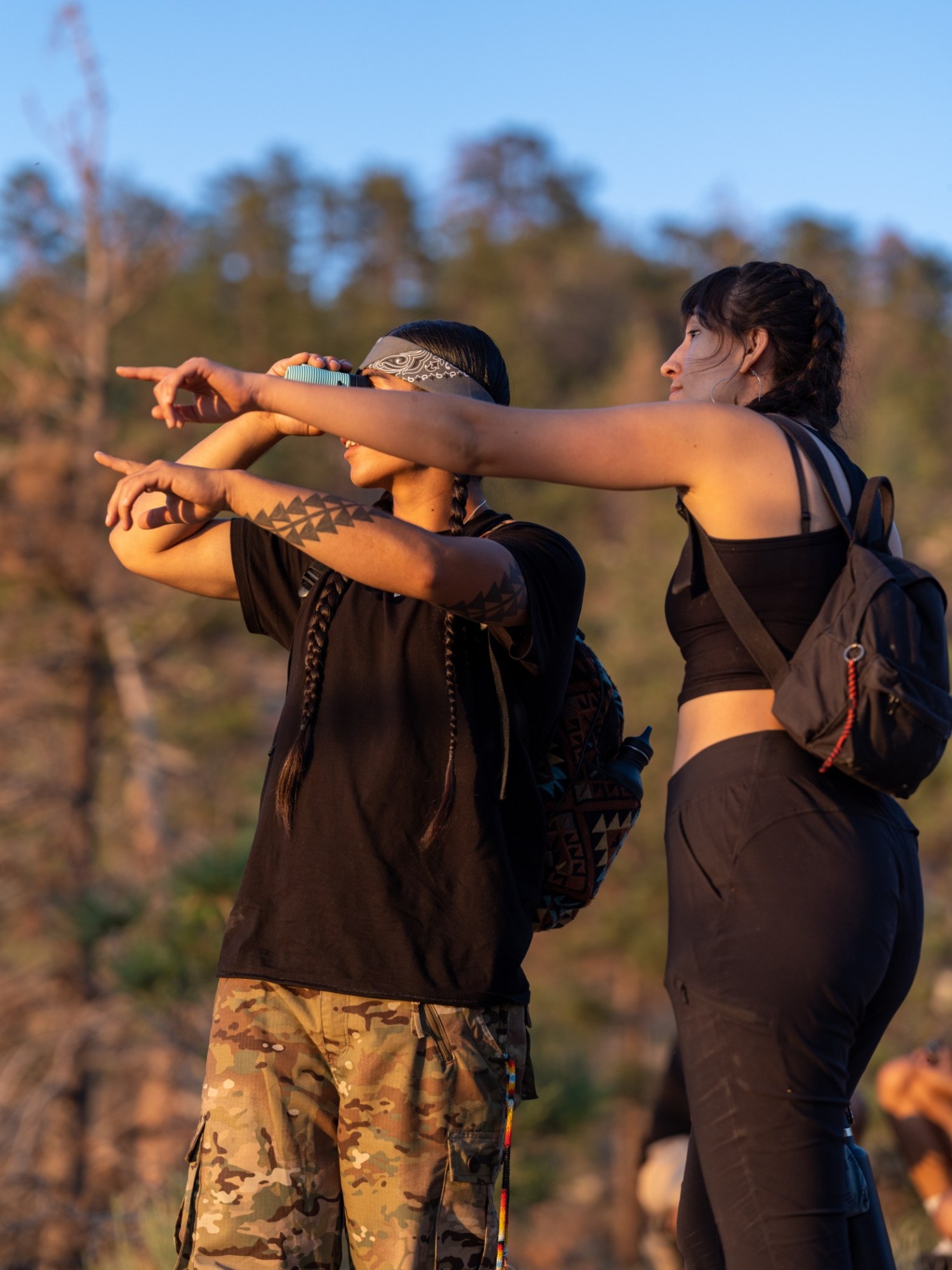 Two people outdoors pointing at something, wearing backpacks.