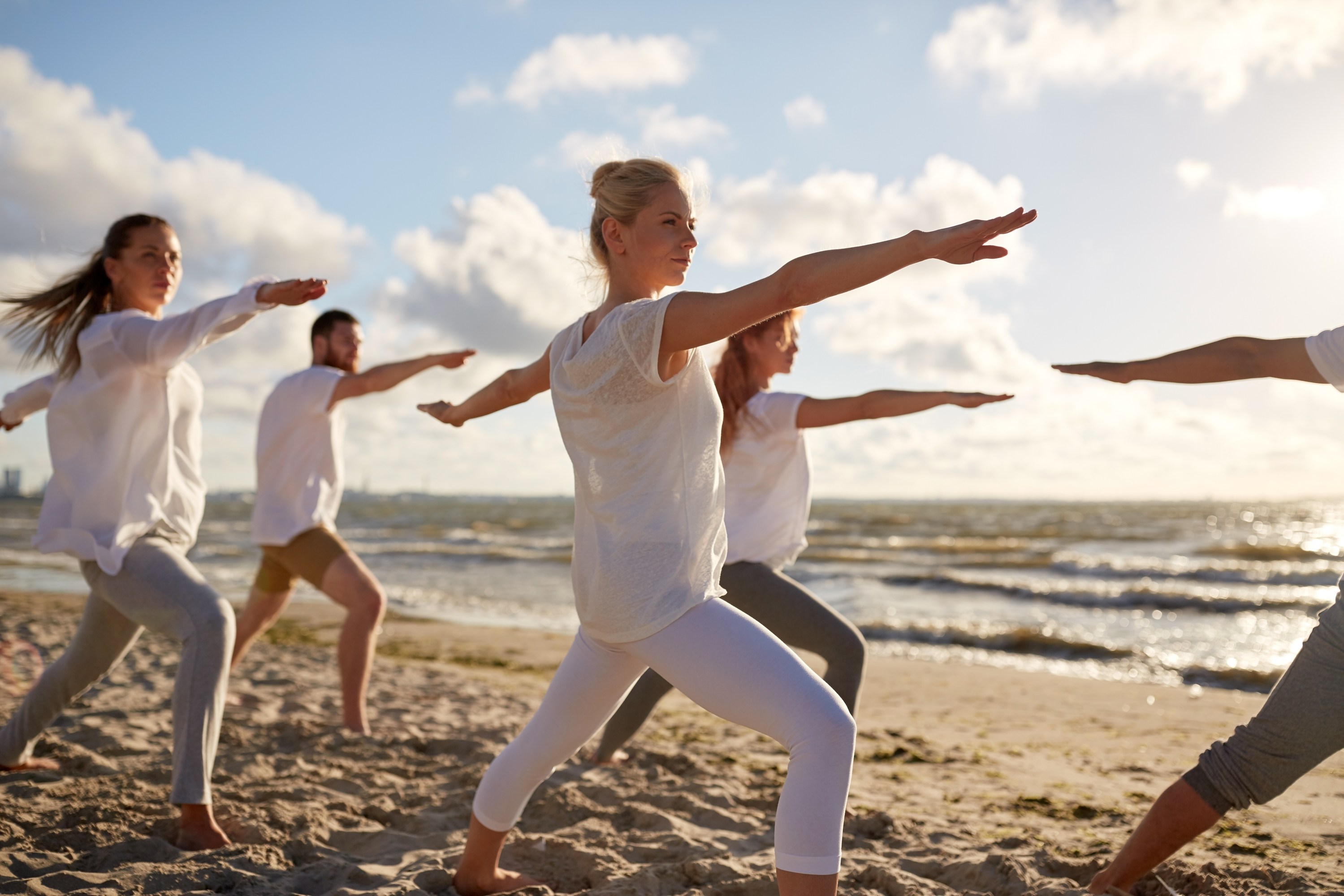Group doing yoga in warrior pose on a sunny beach.