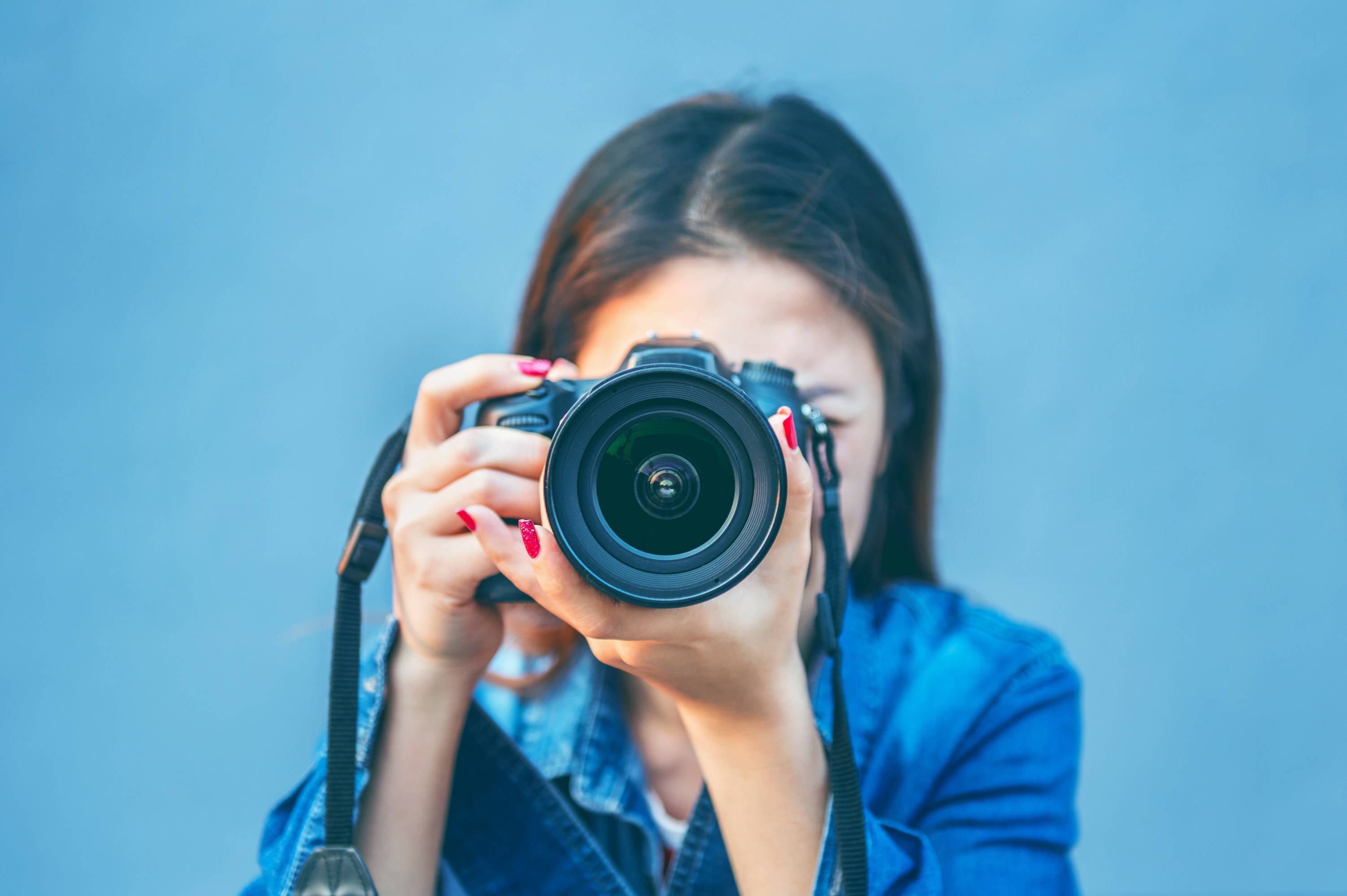 Person in denim holding a camera pointing forward against a plain background.