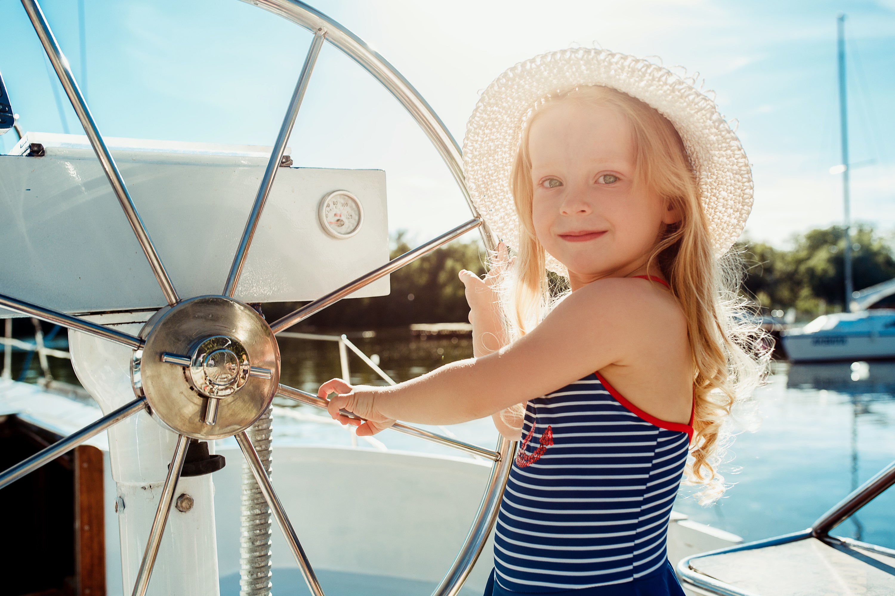 Young girl in a sunhat steering a sailboat wheel on a sunny day.
