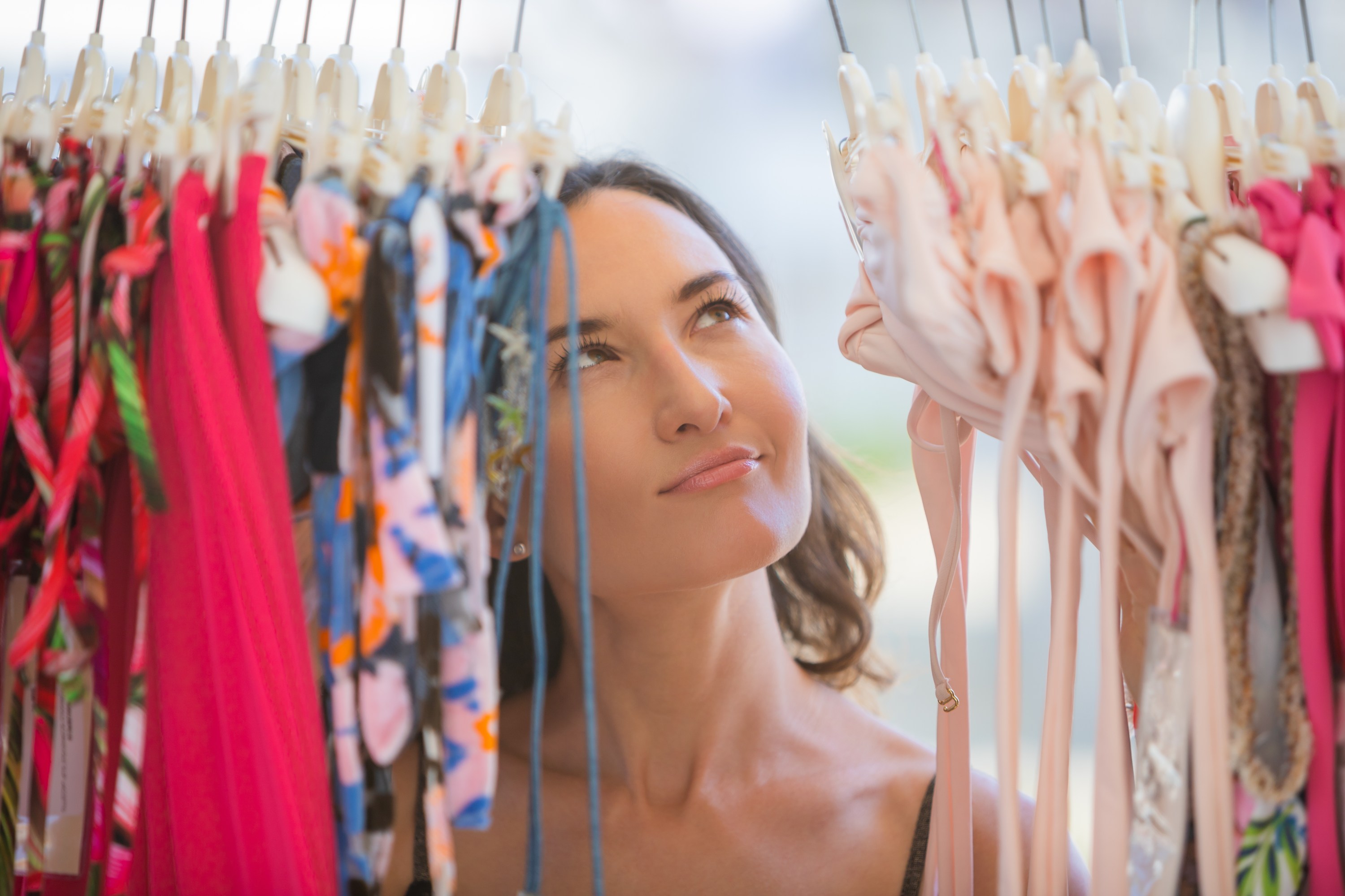 Woman browsing colorful swimsuits on a clothing rack.