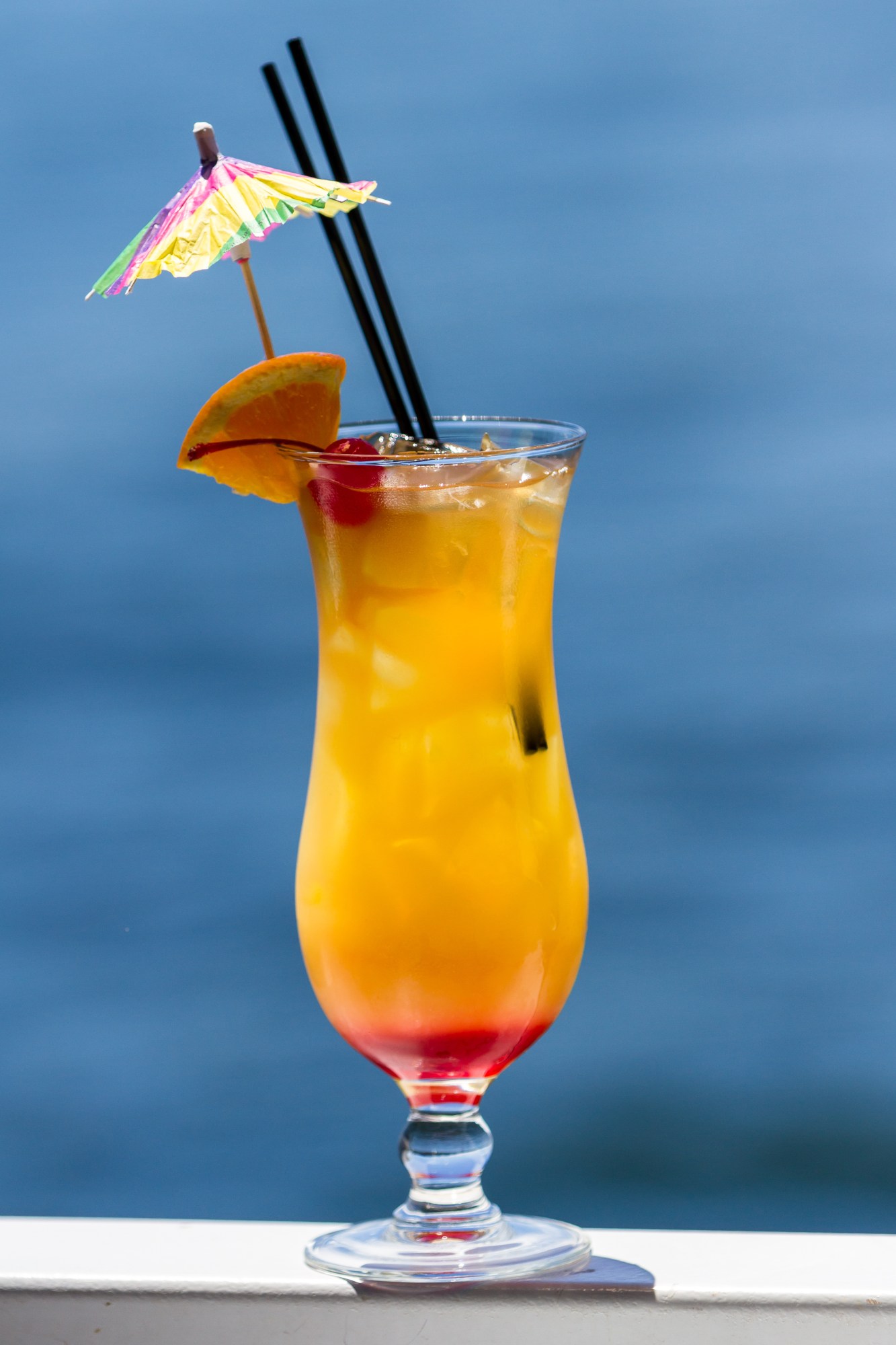 Colorful cocktail with umbrella and fruit garnish near ocean view.