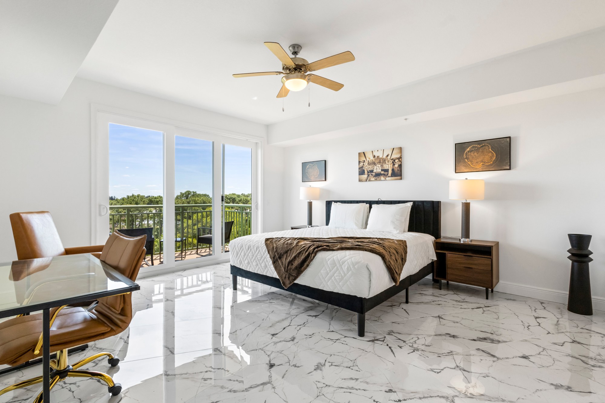 Modern bedroom with bed, glass desk, brown chair, and balcony view.