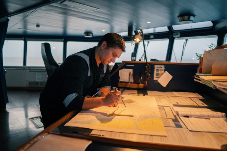 Man plotting a course on a nautical chart in a ship's navigation room.