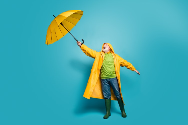 Person in yellow coat and green boots holding a yellow umbrella on a blue background.