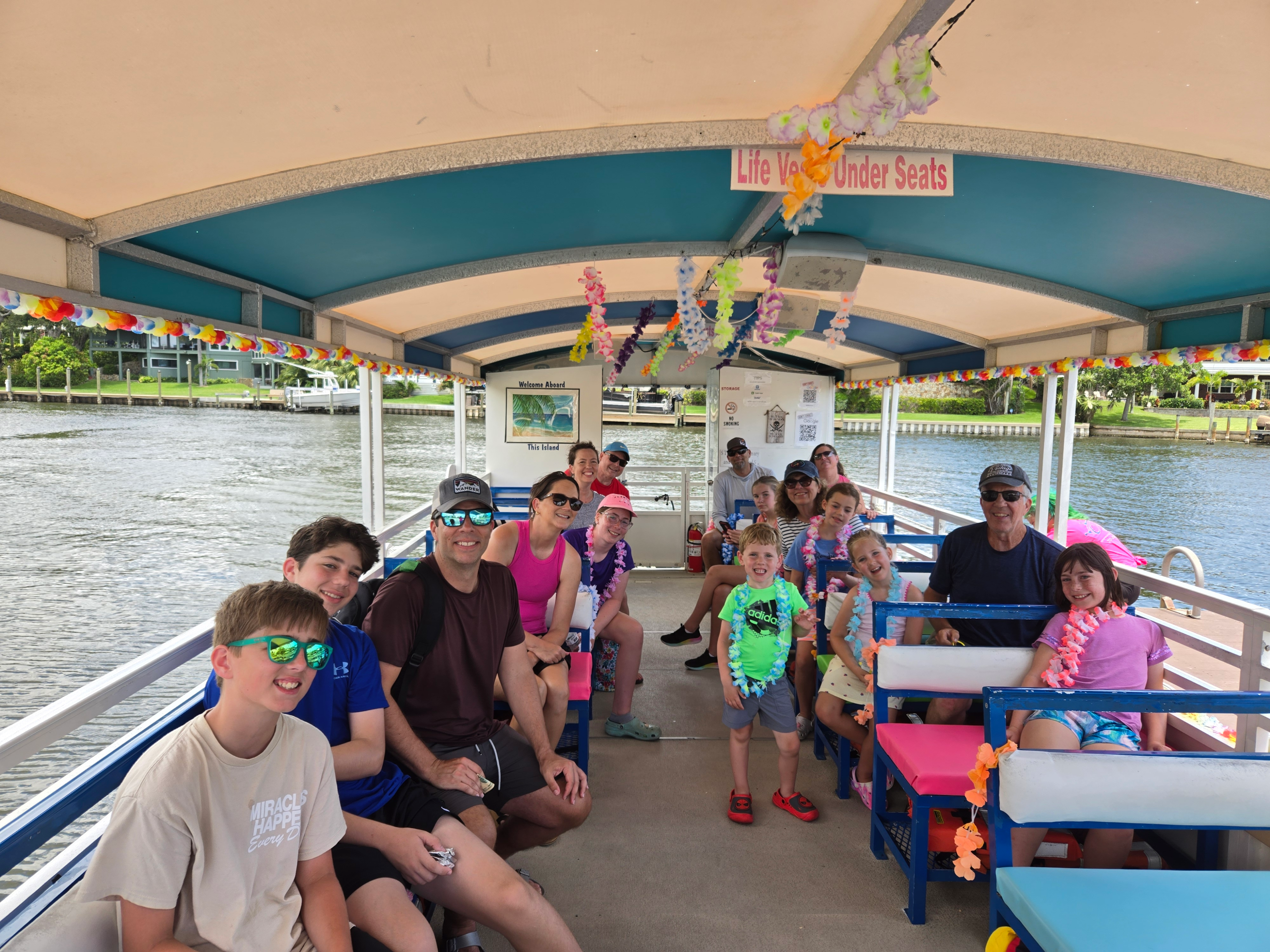 Group of people on a boat, decorated with colorful leis and flowers, enjoying a ride on a sunny day.
