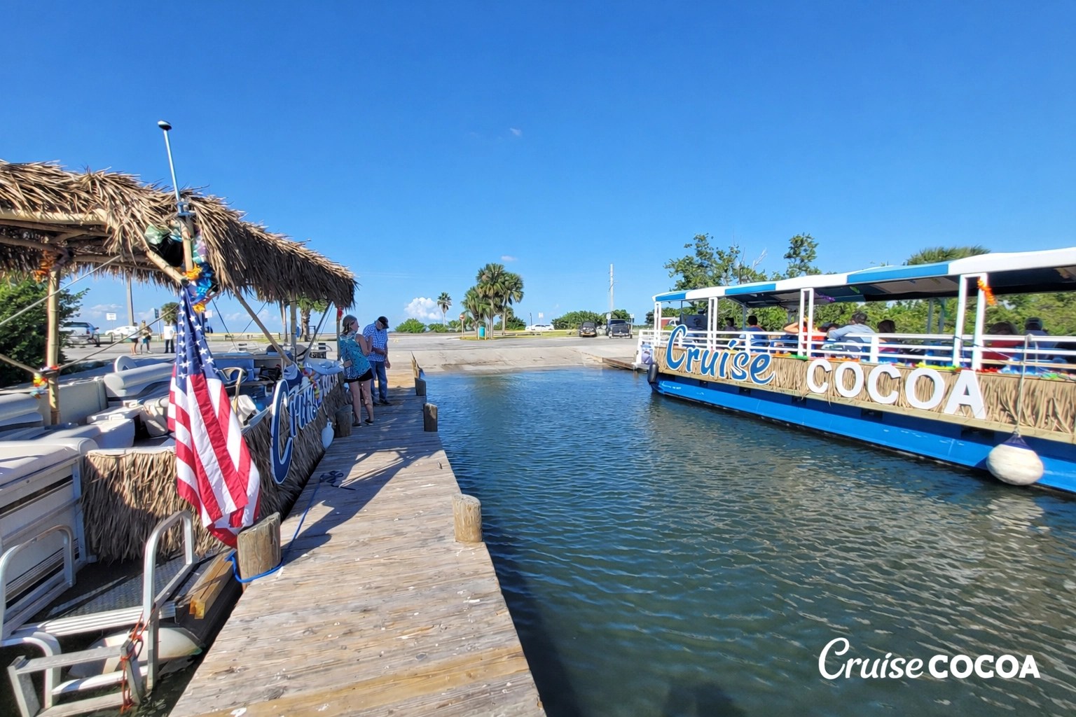 Docked pontoons with thatched roofs, labeled 'Cruise Cocoa,' in a marina under blue sky.