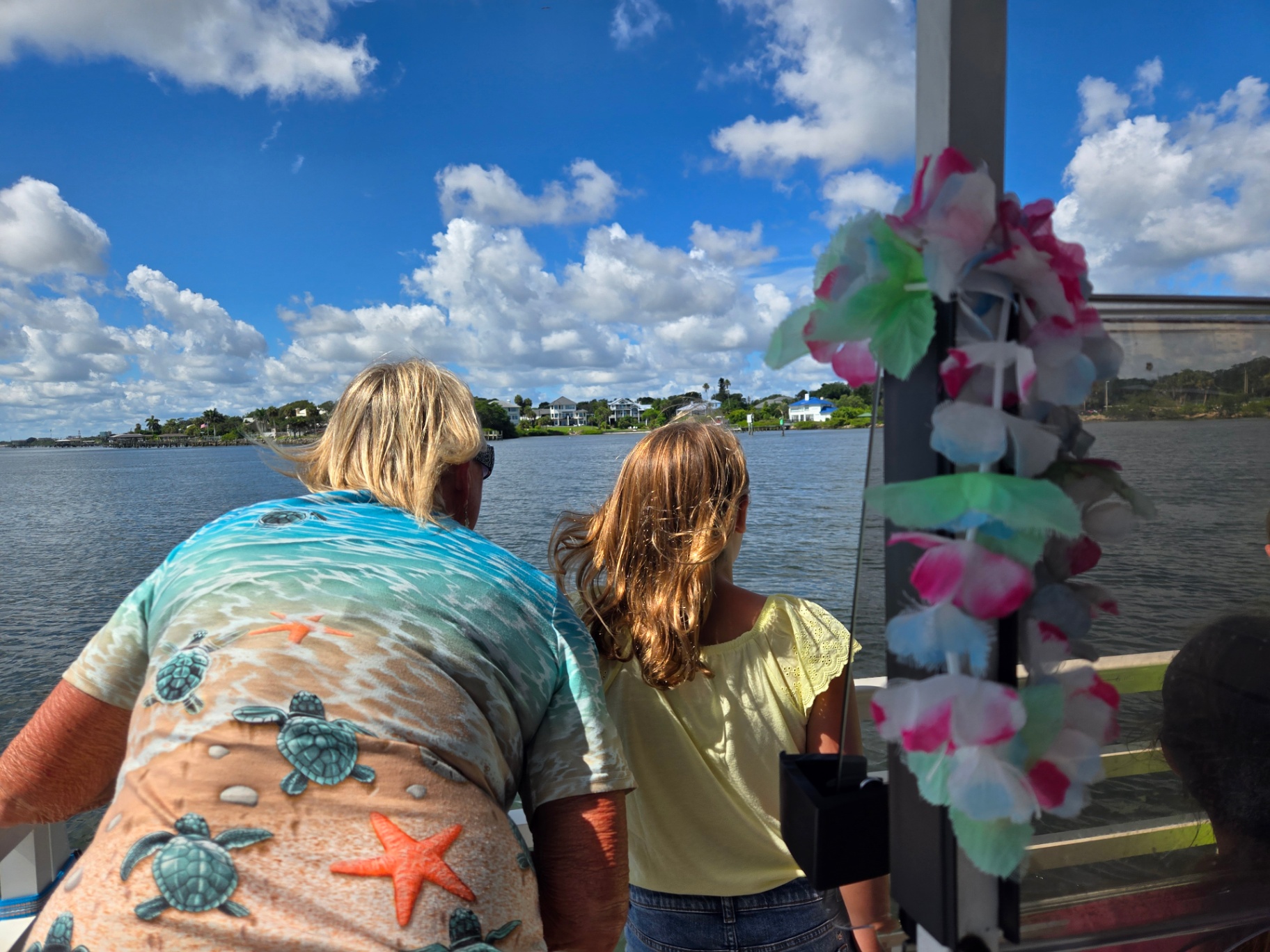 Two people on a boat looking at the water, with colorful lei hanging on the side.