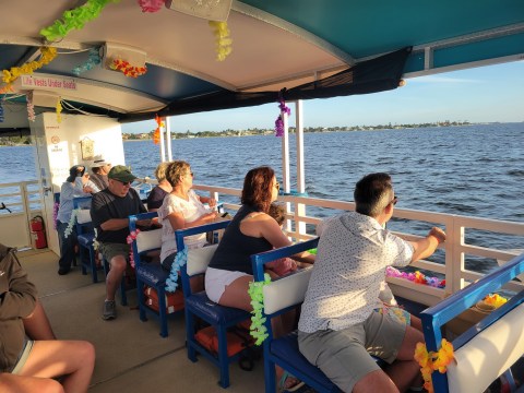 People enjoying a scenic boat ride on sunny day, decorated with colorful leis.