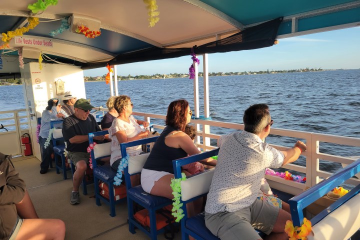 People enjoying a scenic boat ride on sunny day, decorated with colorful leis.