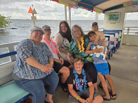 Group of people wearing leis sitting on a boat with a water background.