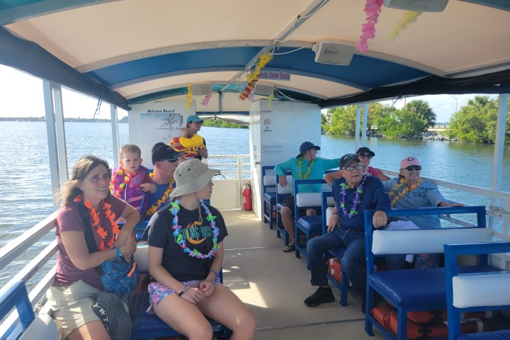 People wearing leis relax on a covered boat in a scenic waterway.