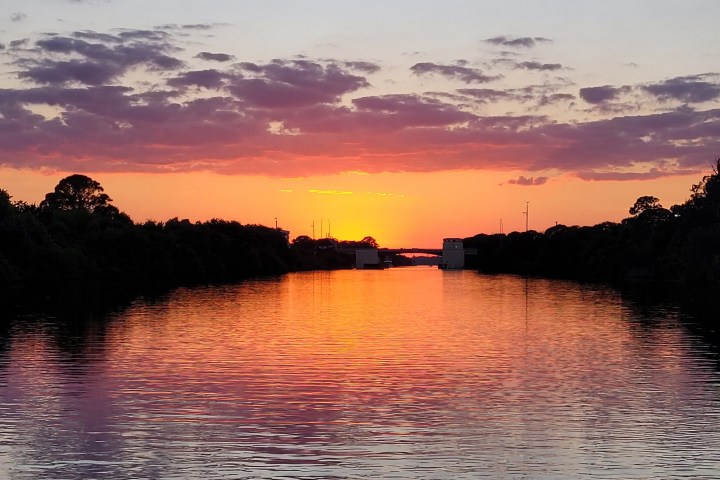 Sunset over a calm river with silhouetted trees and colorful sky.