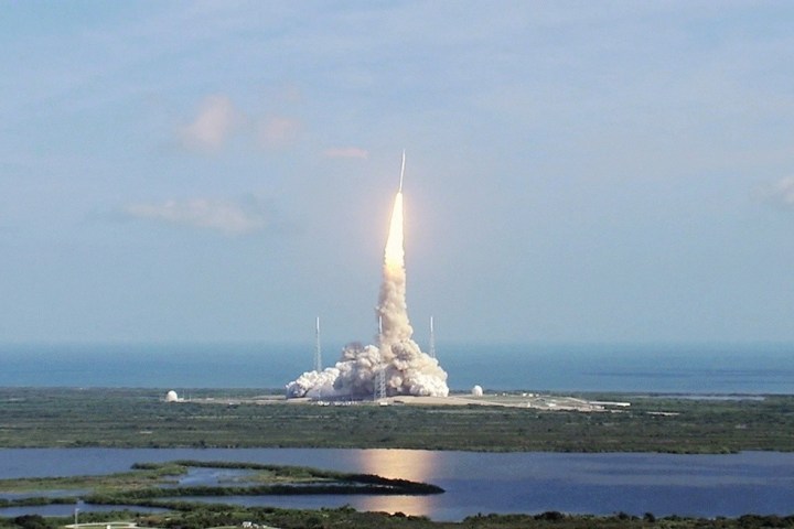 Rocket launch with plume of smoke, ocean and clouds in the background.