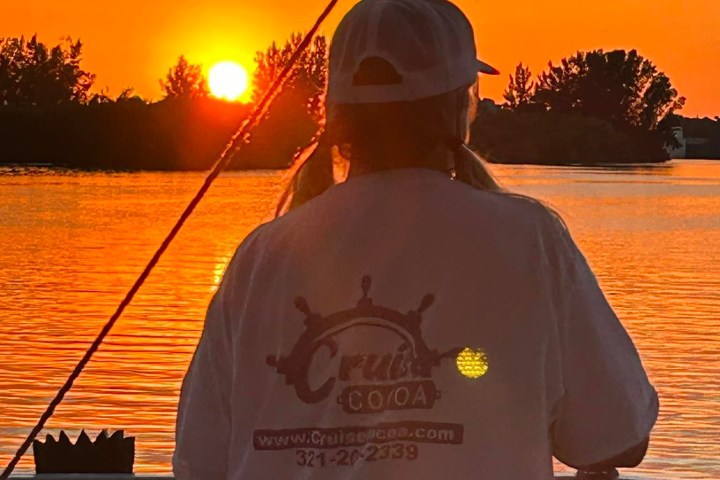 Person in white shirt watching a vibrant orange sunset over a lake.