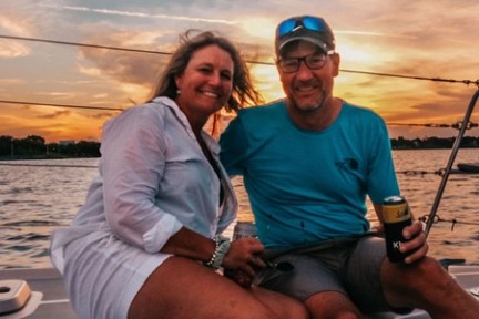 Smiling couple on a boat during sunset, man holding a drink.