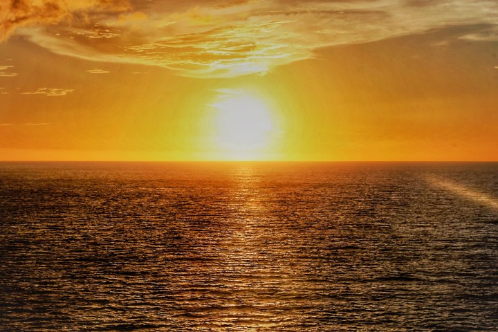 Sunset over ocean with golden sky and textured clouds.